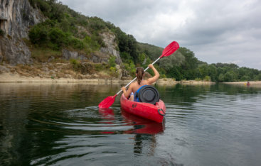 A woman in a red kayak paddling on Blackfoot Reservoir next to the mountains.
